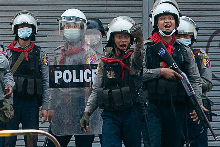 Police gesture toward protesters as security forces crack down on demonstrations against the military coup in Yangon on Sunday. The United Nations says at least 18 protesters were killed Sunday, the deadliest day yet since the military took power earlier this month.