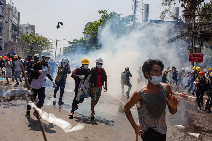 Anti-junta protesters run from teargas fired by police during a demonstration in Yangon on Monday. At least 18 people were killed over the weekend as Myanmar police reportedly used live ammunition against protesters.