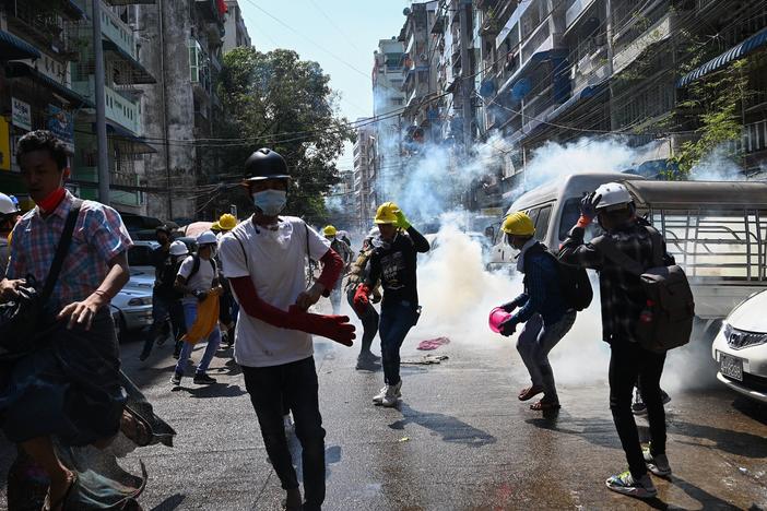 Protesters in Yangon run from police Sunday after they fire tear gas during a demonstration against the military coup.