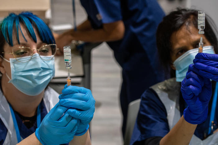 Two health care workers prepare syringes with AstraZeneca's COVID-19 vaccine in London Monday. A U.K. study will expose volunteers to the coronavirus and could help development of future vaccines.
