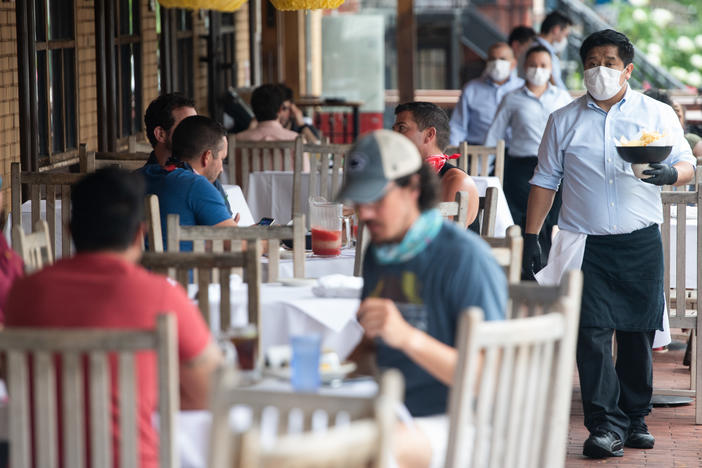 A waiter wearing a mask and gloves delivers food to a table to customers seated at an outdoor patio at a restaurant in Washington, D.C. in May.