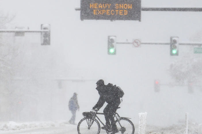 People cross the road as a sign warns of heavy snow on Sunday in Denver, Colo. A winter storm closed roads, impacted flights, and knocked out power in Arizona, Wyoming, Nebraska, and Colorado through the weekend.