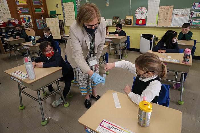 A student gives her coronavirus swab to Helenann Civian, the principal of South Boston Catholic Academy in Boston in January. The White House announced $10 billion to expand testing in K-12 schools.