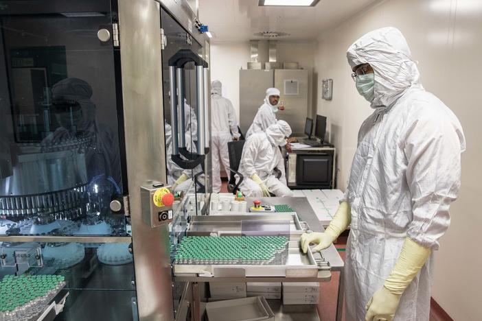 A technician waits to collect vials containing vaccine after they pass through a machine that checks for bottling and vaccine substance deficiencies.