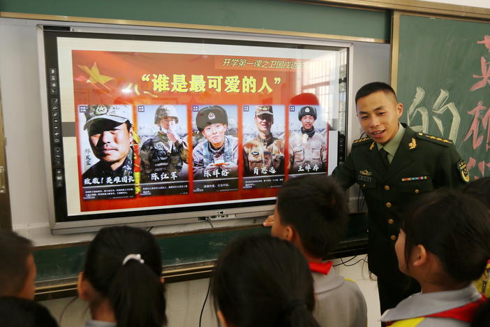 A paramilitary police officer talks next to a screen showing frontier soldiers of the People's Liberation Army during an event at a primary school in Wuzhishan, Hainan province, China, on Feb. 22. On the screen are (L-R) Qi Fabao, who was seriously wounded in the border clash with Indian troops in June last year, and four who were killed: Chen Hongjun, Chen Xiangrong, Xiao Siyuan and Wang Zhuoran.