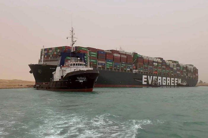 A boat navigates in front of a massive cargo ship that sits grounded after it turned sideways in Egypt's Suez Canal, blocking traffic in a crucial East-West waterway for global shipping. An Egyptian official warned Wednesday it could take at least two days to clear the ship.