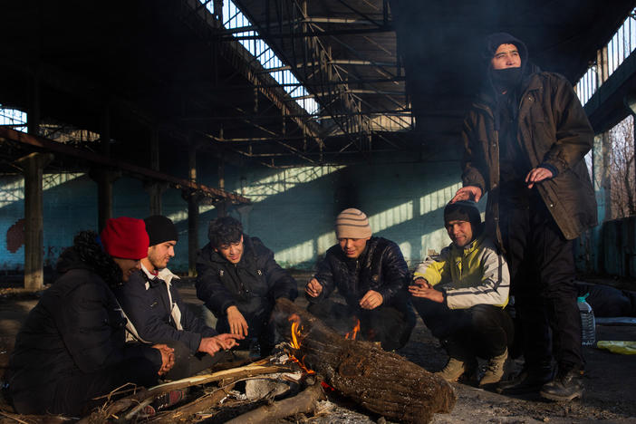 Afghan Morteza Mohammadi (center-left) and his companions sit around a fire in the former Krajina Metal factory in Bihac, Bosnia-Herzegovina, near the Croatian border, discussing possible border crossing strategies related to the weather and time.