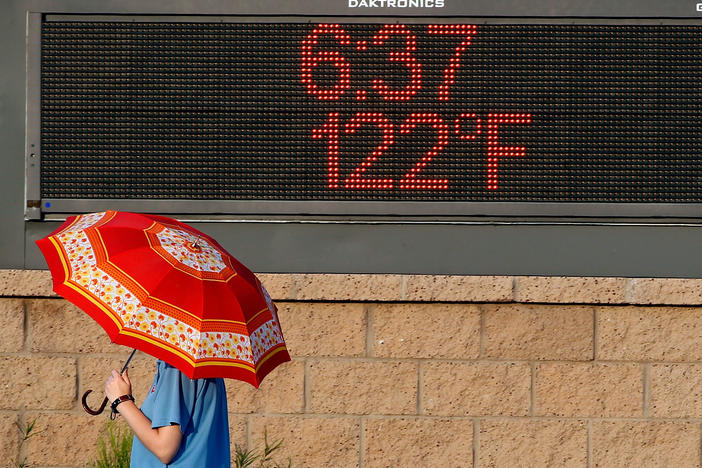 A pedestrian using an umbrella to get some relief from the sun walks past a sign displaying the temperature on June 20, 2017, in Phoenix.