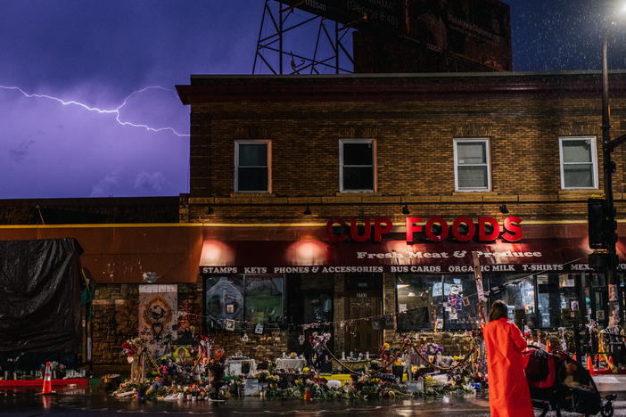 A woman stands with her baby while viewing memorials dedicated to George Floyd in front of the entrance of Cup Foods, the site where George Floyd died.