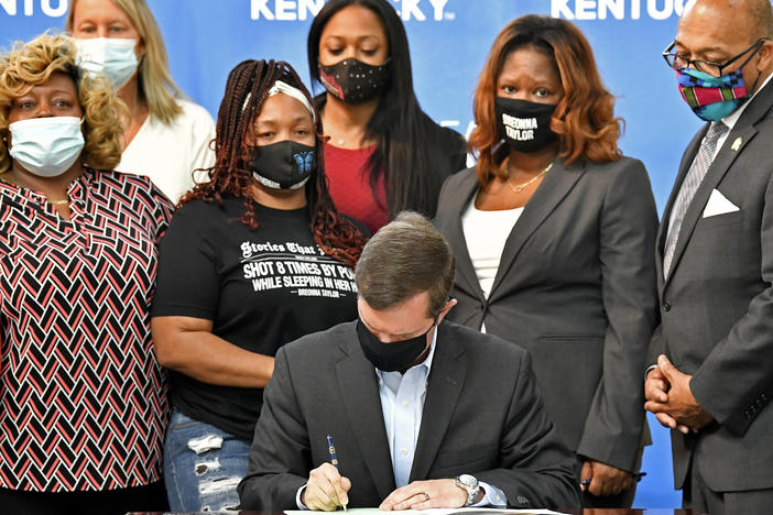 Kentucky Gov. Andy Beshear signs a bill on Friday limiting the use of no-knock warrants statewide. The governor was surrounded by members of Breonna Taylor's family including her mother, Tamika Palmer (standing behind Beshear at left).