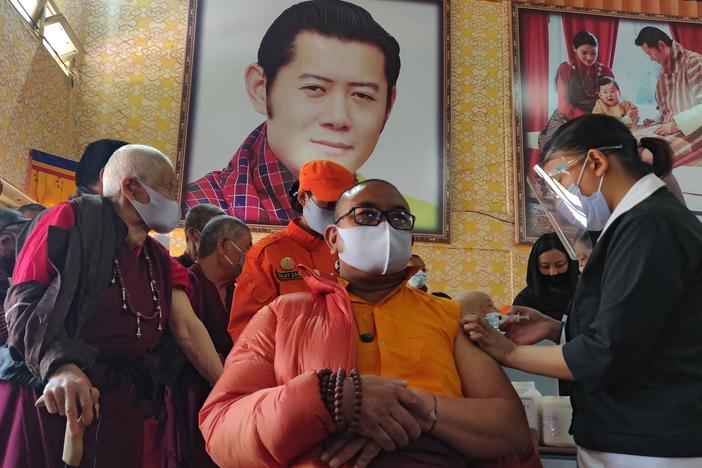 A health worker vaccinates a Buddhist monk sitting in front of a portrait of Bhutanese King Jigme Khesar Namgyel Wangchuck at a secondary school in Bhutan on March 27, the first day of the country's vaccination campaign. Less than two weeks later, health officials said 93% of eligible adults had received their first dose of a COVID-19 vaccine.