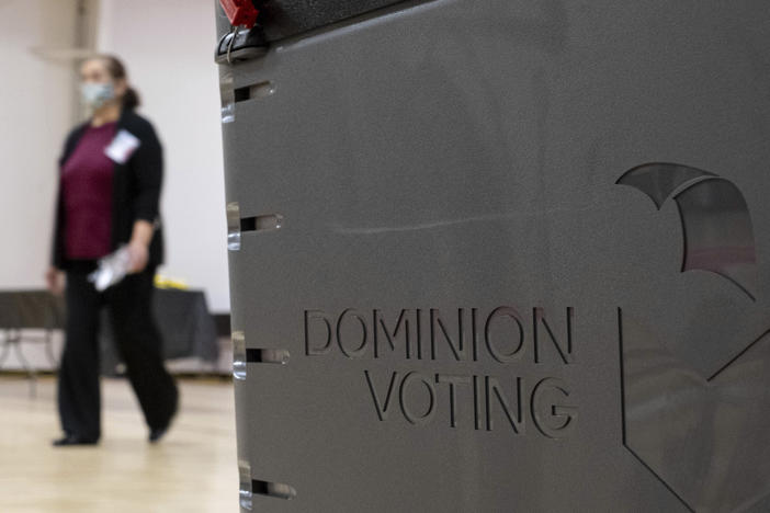 A worker passes a Dominion Voting Systems ballot scanner during Georgia's runoff Senate elections in January in Gwinnett County outside Atlanta. Former President Donald Trump and his allies spread falsehoods about the company's role in the 2020 election, leading to a slew of defamation lawsuits.