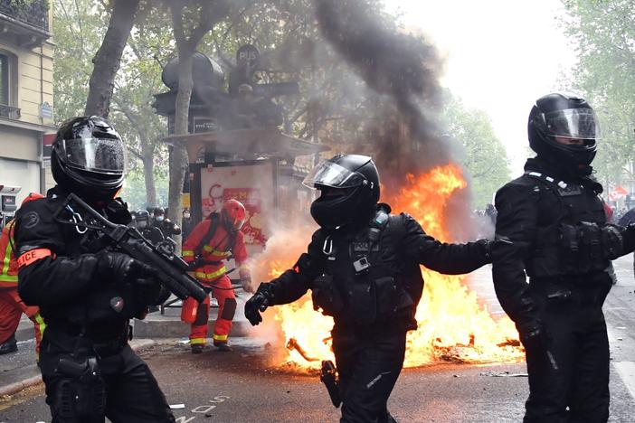 Police officers walk near a fire burning in the street during May Day protests in Paris on Saturday.