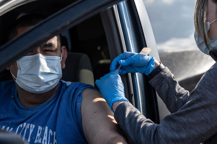 A medical professional from UofL Health administers a vaccine to a patient in their vehicle at University of Louisville Cardinal Stadium.