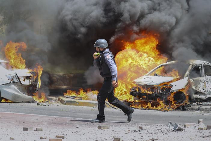 An Israeli firefighter walks next to cars hit by a rocket fired from Gaza on Tuesday in the southern Israeli city of Ashkelon.