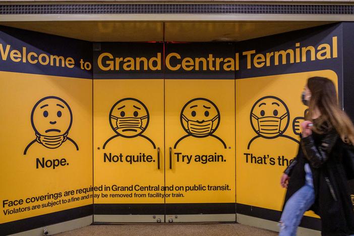 A woman walks past posters explaining mask requirements at Grand Central Terminal train station in New York City on Wednesday. Rules requiring masks on transit are unchanged by the Centers for Disease Control and Prevention's updated mask guidance for fully vaccinated people.