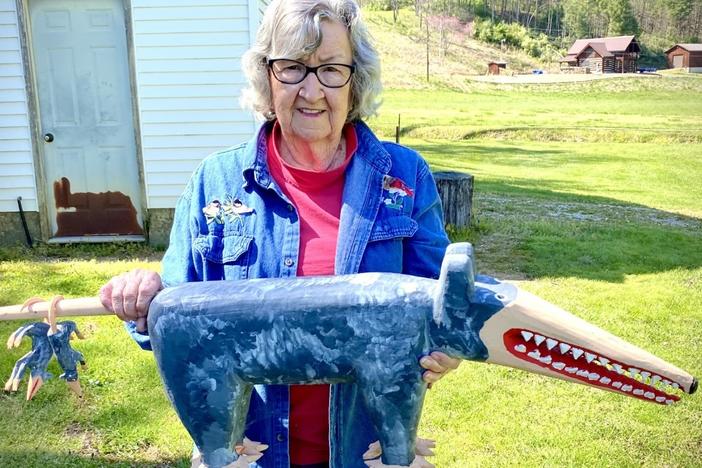 Minnie Adkins stands in her yard in Elliott County, Ky., holding her carving of a possum with baby possums dangling on its tail.