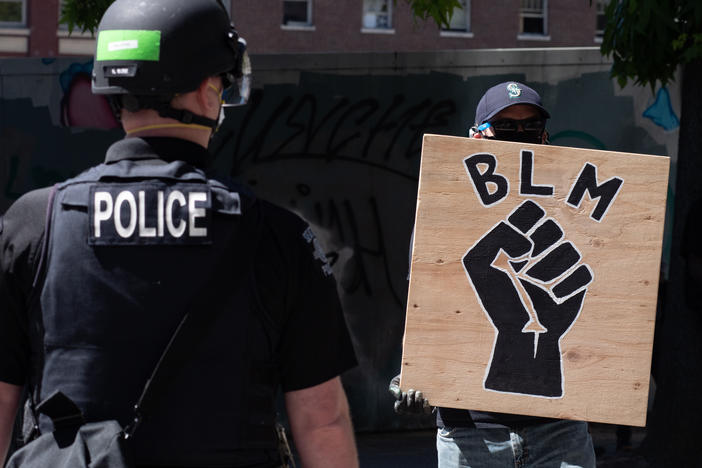 A police officer stands in front of a Black Lives Matter sign during a protest in front of Seattle City Hall on August 9, 2020.