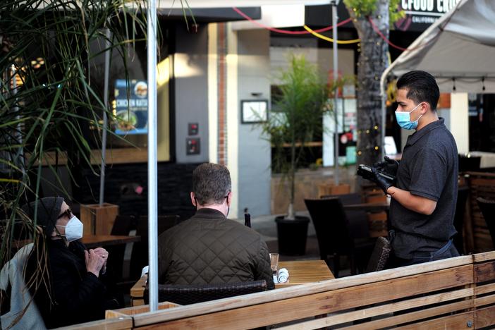 A staff member wearing a mask serves customers at a restaurant in San Mateo, Calif., on May 17.