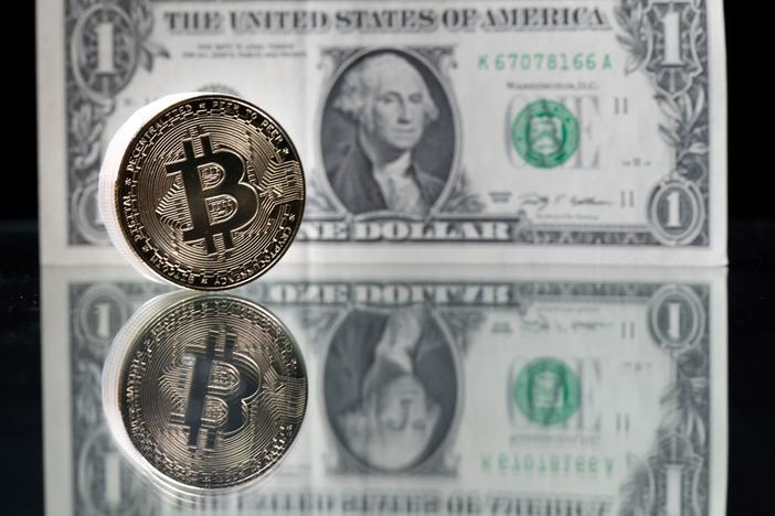 A physical imitation of the Bitcoin cryptocurrency is pictured with a $1 bank note. Cryptocurrencies are plunging over a range of factors, including the spillover impact from falling stock markets and fears about increased regulations.