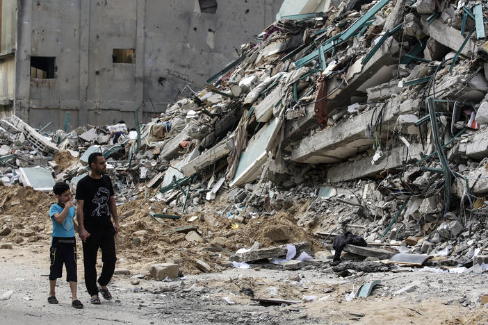 Palestinian people walk past a destroyed tower. (Photo by Ahmed Zakot/SOPA Images/LightRocket via Getty Images)