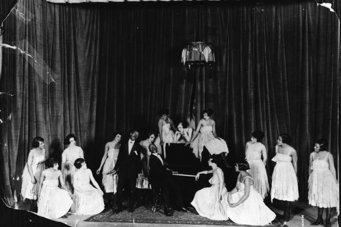 American composers and musicians Noble Sissle, center left, and Eubie Blake, on piano, perform with a group of women on stage in the early 20th century. Sissle and Blake wrote the score for <em>Shuffle Along</em>.