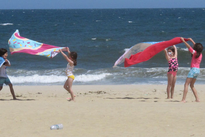 Children play with beach towels on a windy day in Belmar, N.J., on Tuesday. Millions are expected to hit the road or board a plane to celebrate Memorial Day weekend as more people get vaccinated and COVID-19 restrictions are scaled back.