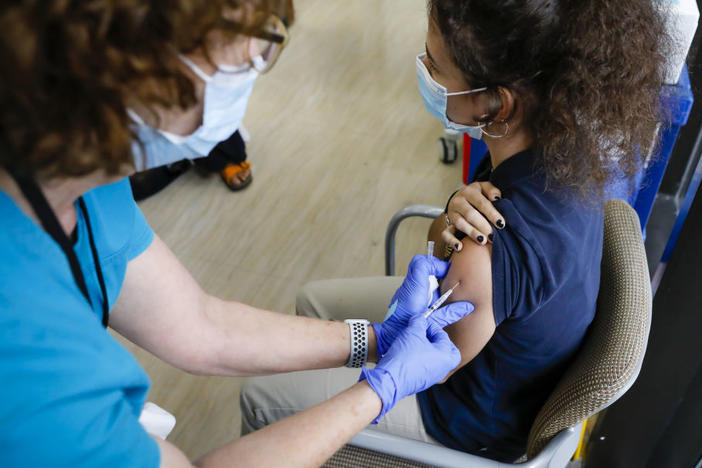 The CDC has softened its guidance for how to operate summer camps for kids this year. Children 12 and older can get the COVID-19 vaccine. Here, a health care worker administers a vaccine dose to a teenager in Miami.