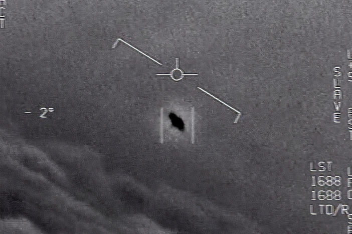In an image from video footage from 2015, an unexplained object is seen at center as it soars among the clouds, traveling against the wind. "There's a whole fleet of them," a naval aviator tells another, though only one indistinct object is shown.
