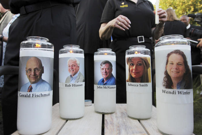In this June 29, 2018, file photo, pictures of five employees of the <em>Capital Gazette</em> newspaper adorn candles during a vigil across the street from where they were slain in the newsroom in Annapolis, Md.