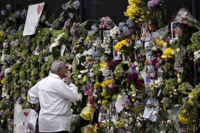 A man looks at a memorial Tuesday with pictures of some of the missing from the partially collapsed 12-story Champlain Towers South condo building in Surfside, Fla.