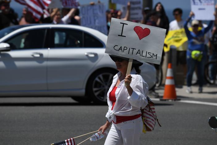 A demonstrator holds a sign reading "I love capitalism" during a protest against California's stay-at-home order in 2020. Capitalism started as an economic system; it has become an ideology in the modern United States.