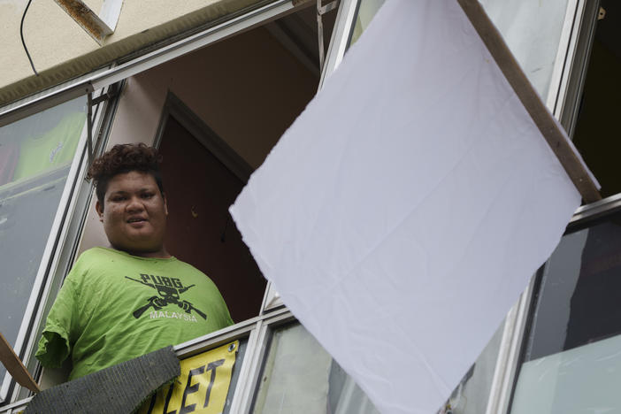 Mohamad Nor Abdullah, born without arms, looks out from a window near a white flag outside the window of his rented room in Kuala Lumpur, Malaysia on July 3. When Mohamad Nor put a white flag outside his window late at night, he didn't expect the swift outpouring of support. By morning, dozens of strangers knocked on his door, offering food, cash and encouragement.