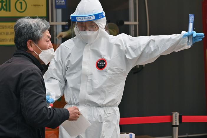 A medical staffer wearing protective gear gestures after collecting a swab from a visitor to test for the coronavirus at a temporary testing station in Seoul in December 2020.  South Korea on Friday announced it would raise restrictions in the capital region to the highest level as a fourth wave of infections is gaining speed.