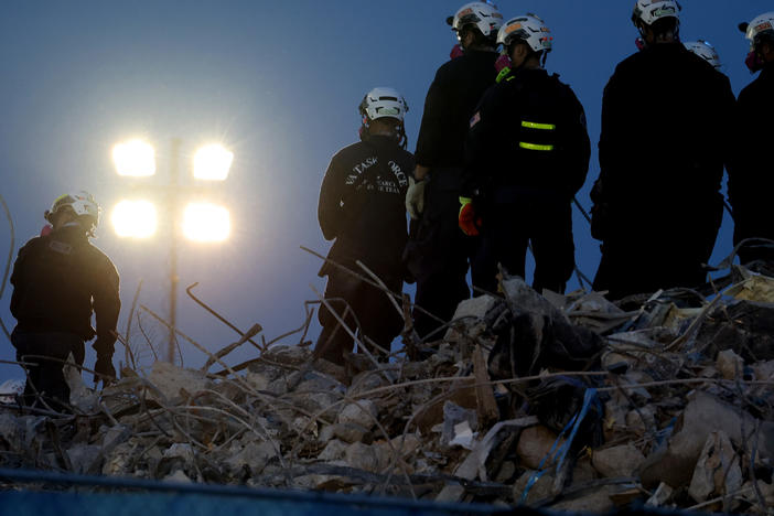 Workers oversee an excavator dig through the rubble of the collapsed 12-story Champlain Towers South condo building on Friday.