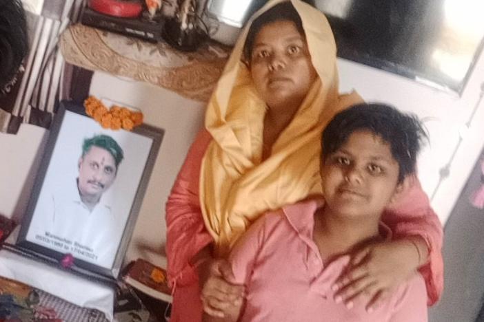 Pooja Sharma (center) and her two daughters, Lata, 14, and Yukti, 12, sit in front of a portrait of Sharma's late husband and the girls' father, Manmohan. He died from COVID-19 in April, leaving Sharma to fend for her family by herself.