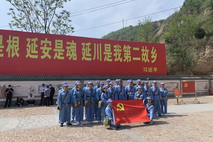 Tourists dressed up as People's Liberation Army soldiers pose in Liangjiahe village, where a teenage Xi Jinping spent seven years doing hard labor. Today the village is a popular red tourism site. The sign displays a quote from Xi: "Liangjiahe is where my roots are, and my soul. It is my second home."