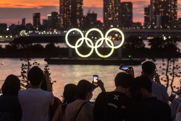 People take pictures as the Olympic rings lit up at dusk on the Odaiba waterfront in Tokyo on Thursday, the eve of the official start of the Tokyo 2020 Olympic Games.
