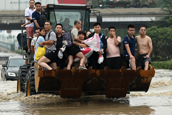 People ride in the front of a wheel loader to cross a flooded street following heavy rains which caused flooding and claimed the lives of at least 63 people in the city of Zhengzhou in China's Henan province on July 23.