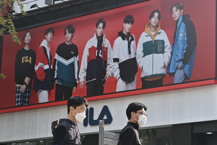 People walk past a poster showing members of the K-pop group BTS in Seoul on October 12, 2020. It's one of the most popular bands in the world, with an extremely devoted fan base.