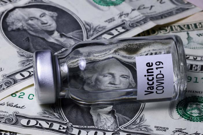 A COVID-19 vaccine vial sits on top of dollar bills.