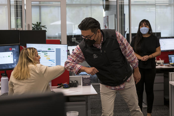 Employees elbow bump at a JLL office in Menlo Park, Calif., in September. With the delta variant surging, mask mandates are returning, and some employers are now requiring employees to be vaccinated before coming to the office.