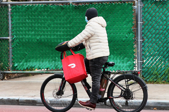 A DoorDash delivery person rides their bike in New York City. Workers across the country went on strike on July 31 to demand higher pay and tip transparency.