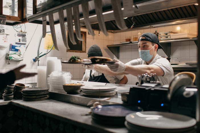 Masked kitchen workers pass plates of food to a server at Claro restaurant in February in New York City. Starting next month, those plates will go only to indoor diners who can prove they have been vaccinated.