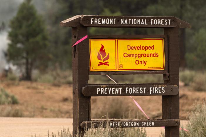 A fire warning sign is seen amid trees which smolder and burn in Division Echo Echo of the Bootleg Fire on July 25, 2021, in the Fremont National Forest of Oregon.