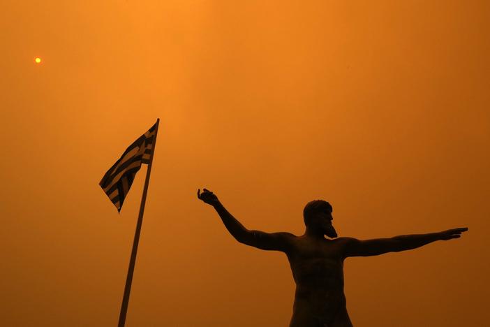 Smoke from wildfire spreads Sunday over the statue of Poseidon, ancient Greek God of the sea, at Pefki village on Evia island, about 118 miles north of Athens.