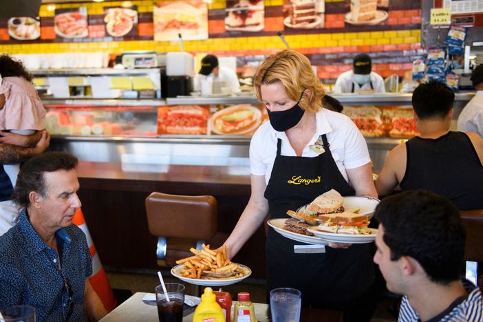 A server delivers food to customers dining at a restaurant in Los Angeles on Aug. 7. Restaurants are boosting pay to attract workers, and that could have an impact on already-high inflation.