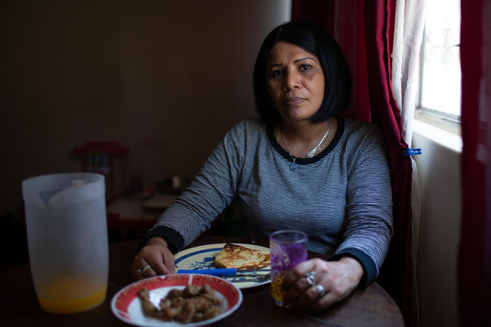 Yroné Camelia Araujo Barreto, a 50-year-old Venezuelan migrant living in Quito, Ecuador, at the dining room table. She is eating a traditional Venezuelan dish of <em>cachapa, </em>round dough made from corn, filled with pork. She typically eats two meals a day if she's lucky enough to afford it.