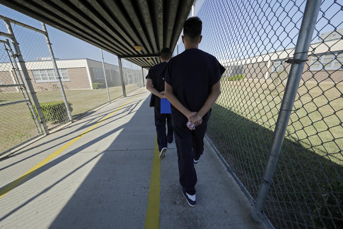 Detainees walk with their hands clasped behind their backs along a line painted on a walkway inside the Winn Correctional Center in Winnfield, La.