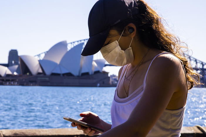 A woman looks at her phone outside the The Royal Botanic Gardens in Sydney, Australia on Aug. 6. The Indicator from Planet Money spoke to an economist for advice on how to cut back on digital dependency.
